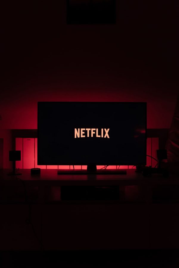 The red and white Netflix logo lights up a black flat screen tv screen in a dark room with red back lighting.