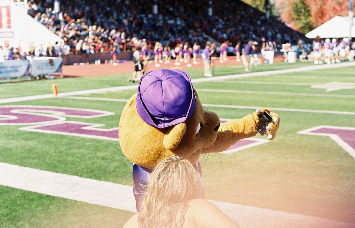 Mac the Wildcat takes a selfie with a cheerleader during the Homecoming Weekend football game. Taken on film.